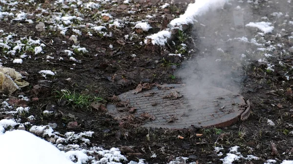 Steam is from sanitary sewer cover in snow, accident. Melted snow around. Close-up view. — Stock Photo, Image