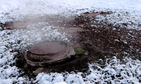 O vapor de close-up é da cobertura de esgoto sanitário na neve no parque de inverno. neve derretida ao redor . — Fotografia de Stock