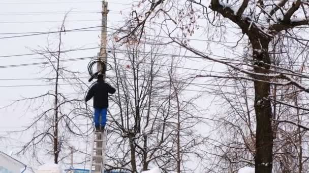 Man repair of power lines in the city in winter. Stands on a ladder with a wire in his hands, back view.