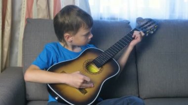 Çocuk kanepede oturan gitar çalmayı öğrenir. Bir müzik aleti çalmayı kavramı.