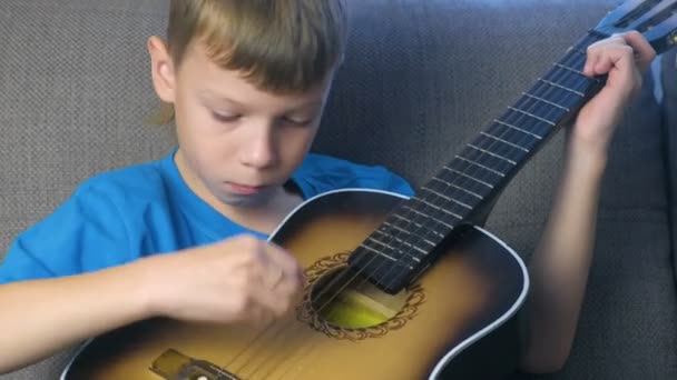Хлопчик дізнається грати на гітарі, сидячи на дивані. Концепція навчитися грати на музичних інструментах. — стокове відео
