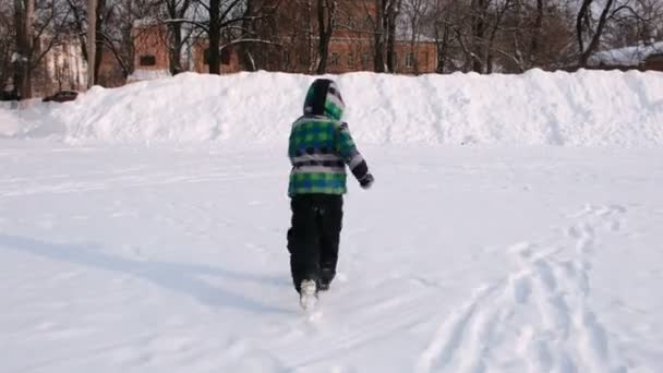 El chico juega en la nieve. Corre y sube a una alta deriva de nieve . — Vídeo de stock