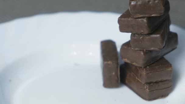 Falling tower of a chocolate candies on a white plate. Concept of unhealthy eating. — Stock Video