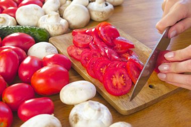 Kadının mutfak masasının üzerinde ahşap bord üzerinde kesme domates var. Yan görünüm.