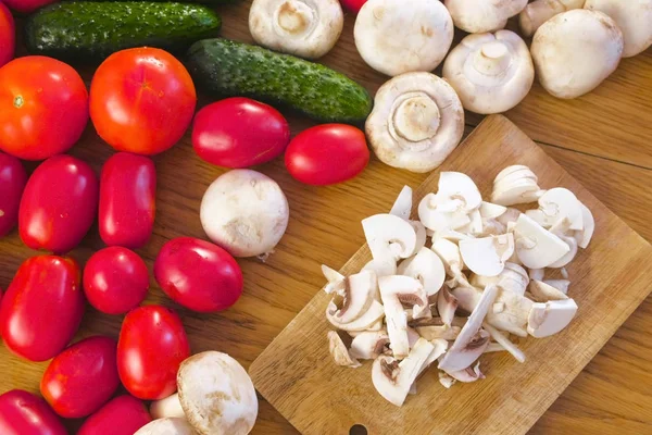 Cortar champiñones champiñones sobre tabla de madera sobre mesa de cocina con diferentes verduras . — Foto de Stock