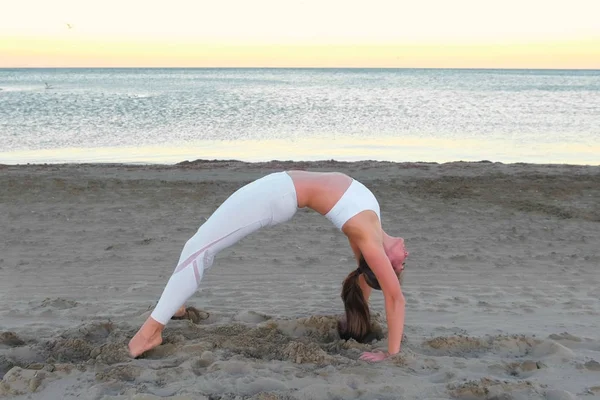 Молодая женщина занимается йогой Dhanurasana Боу Поза на песчаном пляже на рассвете осенью . — стоковое фото