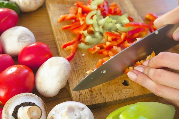 Mujeres manos pelan pimiento verde sobre tabla de madera en la mesa de la cocina con verduras . — Foto de Stock