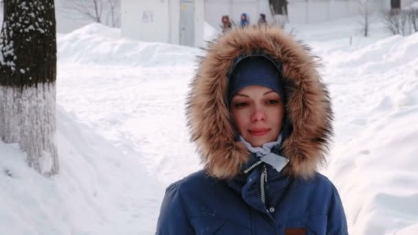 Primeros planos sonriente mujer está caminando en el parque de invierno en la ciudad durante el día en clima nevado con nieve que cae. Vista frontal — Vídeos de Stock