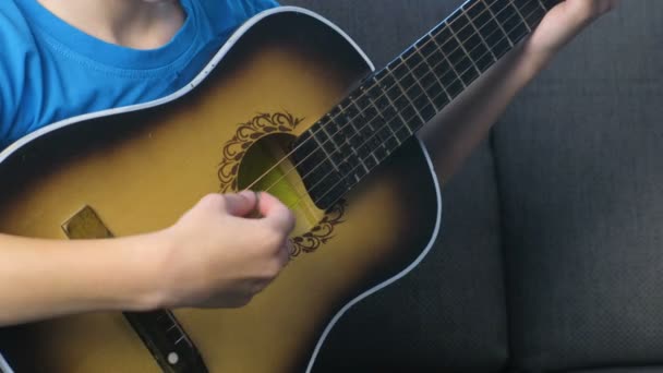 Boy is playing guitar sitting on the couch, hands close-up. Concept of learning to play a musical instrument. — Stock Video