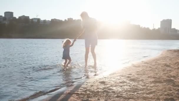 ママと夕日と泳ぐ」で川のビーチで遊ぶ女の子. — ストック動画