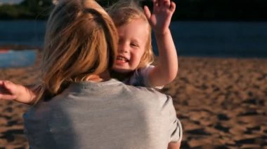 Güzel mutlu sarışın anne ve kızı sarılma ve gün batımında sahilde konuşma.