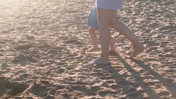 Beautiful blonde mom and daughter walk on the beach at sunset. Close-up legs. — Stock Video