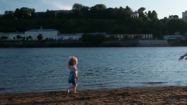 Bella bionda mamma e figlia corrono verso l'altro sulla riva del fiume al tramonto . — Video Stock