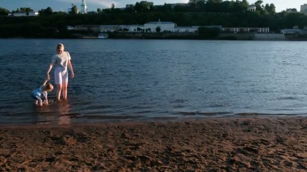 Mamá y niña jugando en la playa del río al atardecer y nadar . — Vídeos de Stock