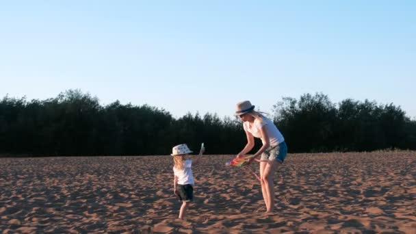 Hermosa rubia en un sombrero mamá e hija lanza una cometa en la playa . — Vídeos de Stock