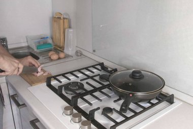 Gaz sobası yakınındaki mutfakta ahşap bir gemide sosis kesilmiş eller mans.