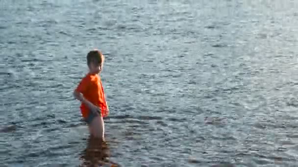 Garçon en t-shirt rouge marche sur l'eau de la rivière . — Video