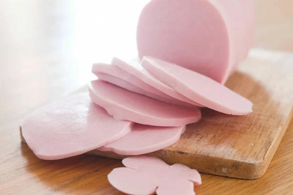 Slices of a boiled sausage on wooden cutting board on the kitchen table. — Stock Photo, Image