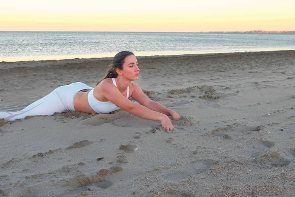 Mujer joven está haciendo yoga sentado en una cuerda cruzada en la playa de arena al amanecer . —  Fotos de Stock