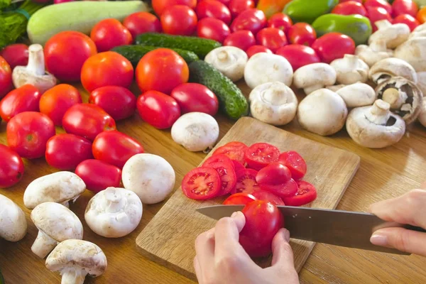 Womans manos está cortando tomates en la caldera de madera en la mesa de la cocina. Vista lateral . — Foto de Stock
