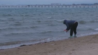 Yaşlı kadın gezgin deniz bir şişe su kumlu bir plaj üzerinde duran kazanıyor. Deniz kıyısı sonbaharda. Deniz Hediyelik eşya.