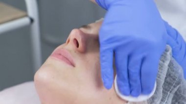 Güzellik uzmanı Pamuklu ped ile genç bir kadın yüzü siliyor. Şevval özçelik güzellik eldiven ve bir yüz closeup elleri. Güzellik bakımları yüz için.