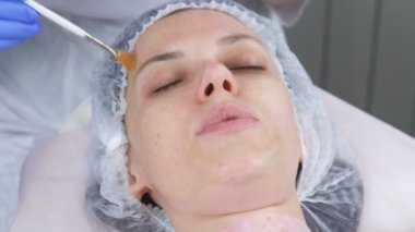 Şevval özçelik güzellik bir fırça ile kadının yüzünde bir maske koyar. Güzellik uzmanı mavi kauçuk eldiven eller. Yüz bakımları.