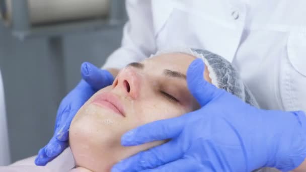 Kosmetolog gäller en löddrande rengöring för ansiktet av kunden om en ung kvinna. Ansikte och händer närbild. — Stockvideo