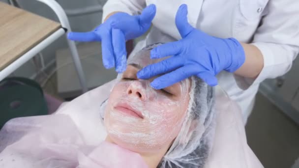 Kosmetolog rullar masken på kvinnans ansikte massagerörelser. Kosmetolog ansiktsbehandling. — Stockvideo