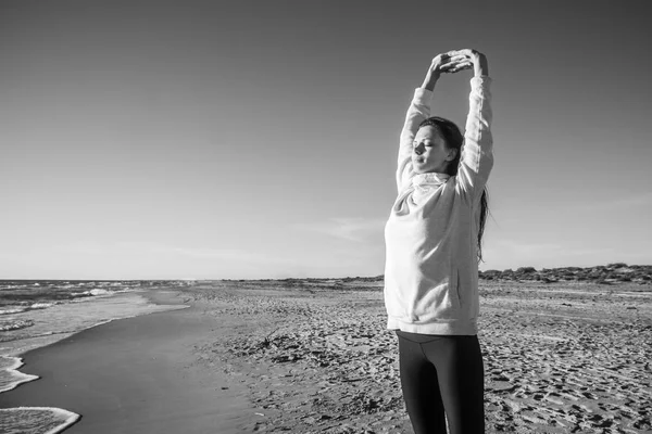 Женщина растягивает занятия йогой на песчаном пляже волнами. Черное и белое . — стоковое фото