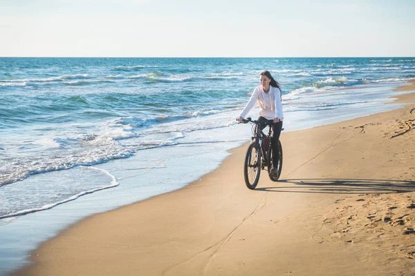 若い女性の美しい砂浜のビーチで海に沿って自転車に乗る. — ストック写真