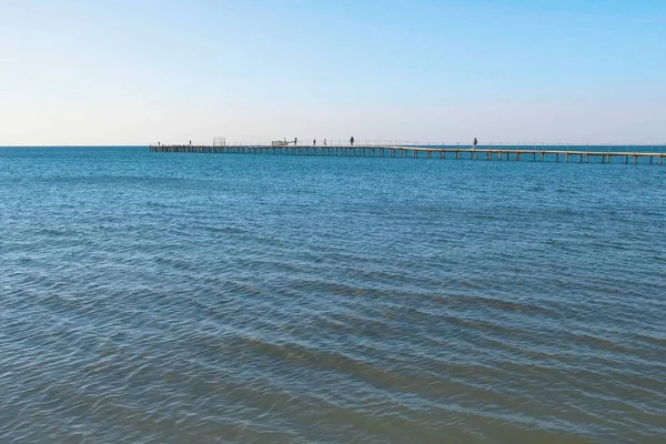 Menschen gehen auf einem alten Holzsteg im Meer spazieren. Seitenansicht. — Stockfoto