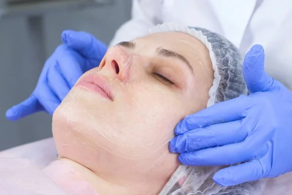 Kosmetolog anvender en skummende sæbe til ansigtet af klienten hos en ung kvinde. Ansigt og hænder close-up . - Stock-foto