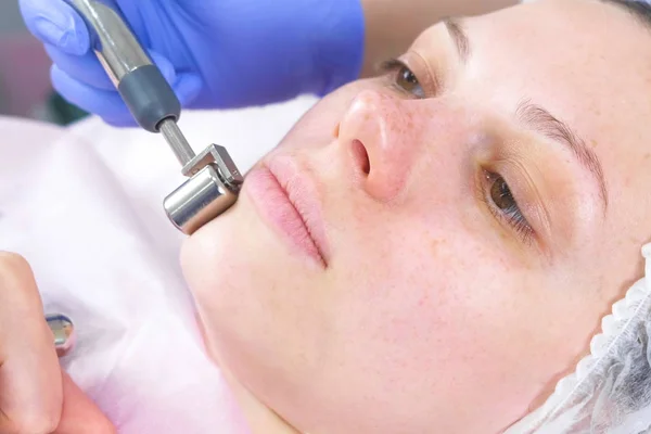 El cosmetólogo hace un procedimiento micro-actual para la cara de una mujer joven. Cara de cerca, vista lateral . — Foto de Stock