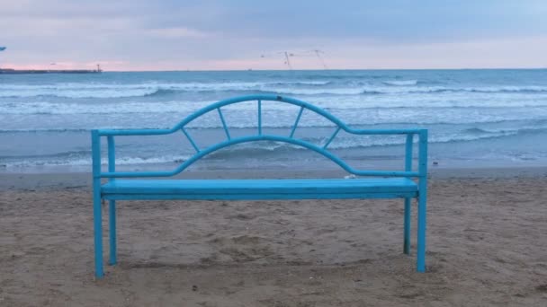 Blaue Bank am Sandstrand bei Sonnenuntergang. bequeme Infrastruktur zum Entspannen am Meer. Meereswelle. — Stockvideo