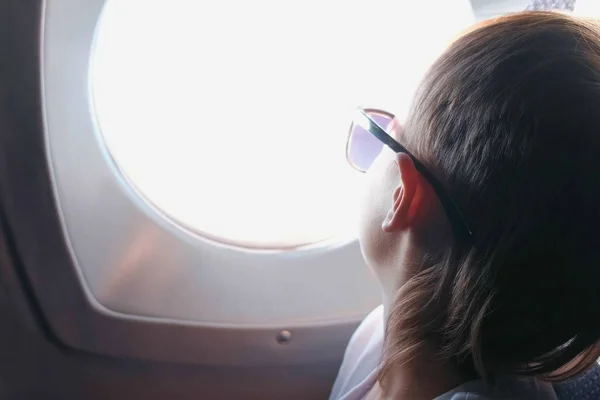 Junge schaut mit Sonnenbrille aus dem Flugzeugfenster. — Stockfoto
