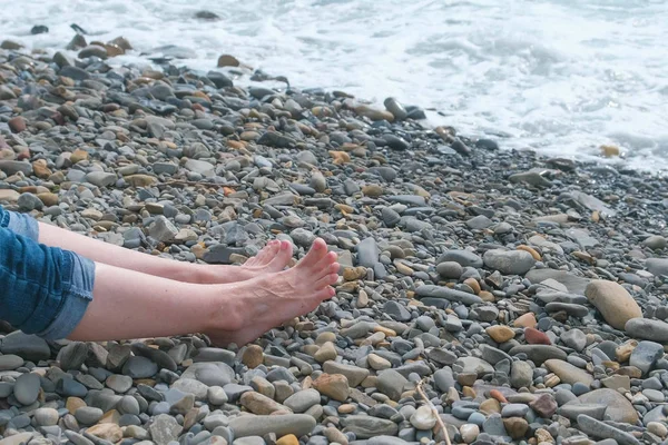 Mujeres pies en jeans contra el mar en la playa de piedras . — Foto de Stock