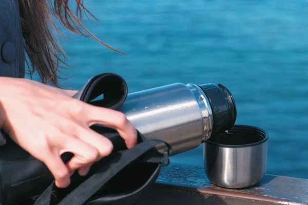 Kobieta, zalewanie herbaty z termos na nabrzeżu. Młoda brunetka w podróż. Wirydarz-do góry ręce. — Zdjęcie stockowe