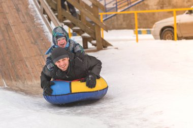 Baba ve oğul karlı slayt üzerinde bir boru içinde haddeleme.