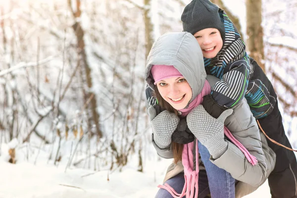 Feliz sonriente madre e hijo tienen un abrazo en medio del juego en el bosque de invierno . — Foto de Stock