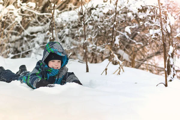 Lyckligt leende pojke liggande i snön i vinter skogen. — Stockfoto