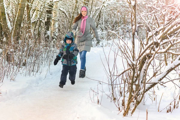 Hermosa madre joven caminando con su hijo en el bosque de invierno. Ponerse al día . — Foto de Stock
