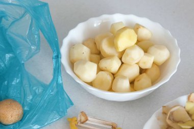 Küçük patatesler plaka, kabuğu ve soyucu mutfak masasının üzerinde. Plastik mavi çanta üzerinde unpeeled patates.