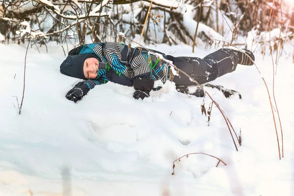 Menino sorridente feliz deitado na neve na floresta de inverno . — Fotografia de Stock