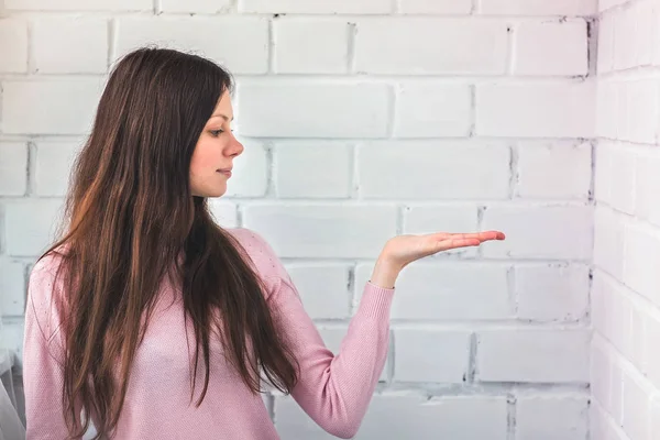 Beautiful woman stands a white brick background and keep on something on her hand and look on it. — Stock Photo, Image