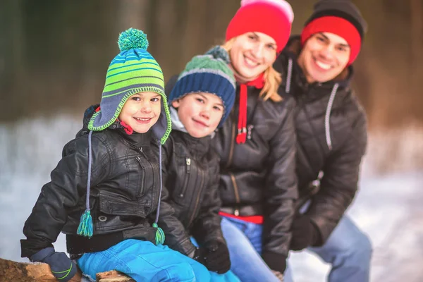 Retrato de familia feliz en el bosque de invierno sentado en el tronco . — Foto de Stock