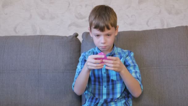 Happy boy is putting a pink slime on his hand sitting on the coach and playing. — Stock Video