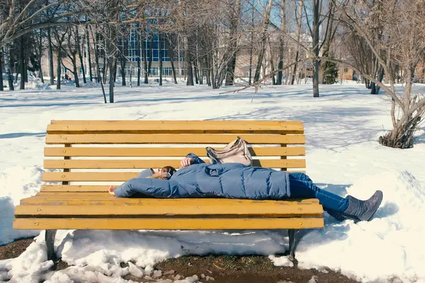 Уставшая молодая женщина зимой спит в парке на скамейке запасных . — стоковое фото
