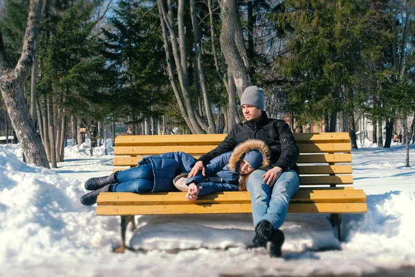 Homem e uma mulher descansam juntos em um banco no parque da cidade de inverno. Dia de inverno ensolarado . — Fotografia de Stock
