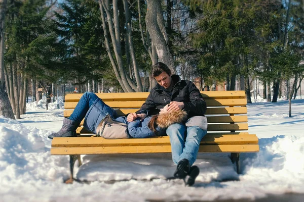 Homem e uma mulher descansam juntos em um banco no parque da cidade de inverno. Dia de inverno ensolarado . — Fotografia de Stock